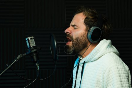 Téléchargez les photos : Chanteur masculin passionné avec écouteurs effectue en studio d'enregistrement insonorisé - en image libre de droit