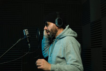 Focused male sound producer with headphones records vocals in a soundproof recording studio