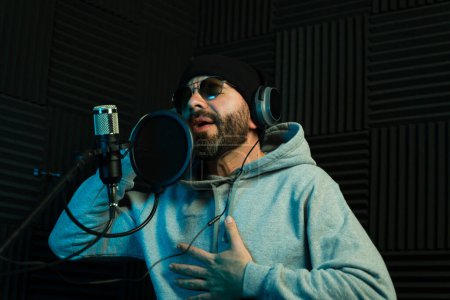 Focused male singer with headphones performs energetically in a soundproof recording studio