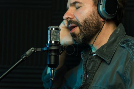 Close-up of a man singing into microphone with headphones in a soundproof recording studio
