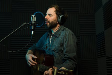 El hombre toca la guitarra y canta en un micrófono en un estudio de grabación insonorizado