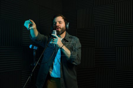 Male singer with headphones recording a song, standing in a soundproofed studio