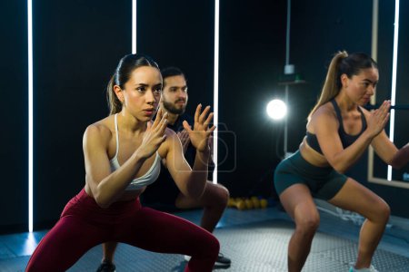 Téléchargez les photos : Hommes et femmes concentrés faisant des exercices de squat lors d'une séance d'entraînement de groupe - en image libre de droit