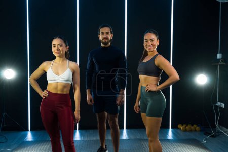 Drei fitte Trainer posieren in einem Fitnessstudio, bevor sie eine Fitnesseinheit beginnen