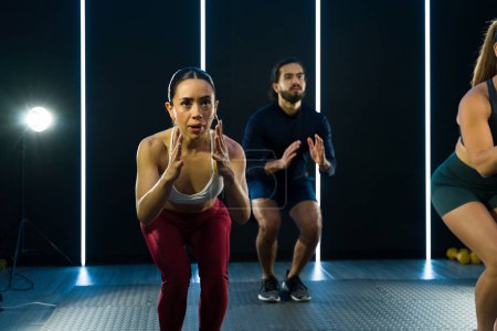 Téléchargez les photos : Individus concentrés effectuant des squats dans un cadre de cours de conditionnement physique moderne - en image libre de droit