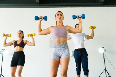 Foto de Tres personas enfocadas levantando pesas juntas en un brillante gimnasio - Imagen libre de derechos