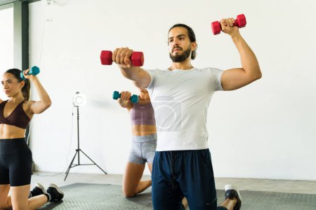 Téléchargez les photos : Des hommes et des femmes concentrés soulevant des poids ensemble dans un cours de gym - en image libre de droit