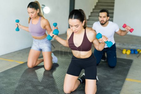 Photo for Three friends engage in a synchronized dumbbell exercise during a fitness class - Royalty Free Image
