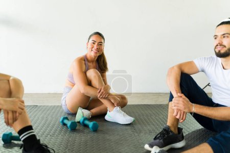 Gruppe unterschiedlicher Menschen lächelt und ruht während eines Fitnesskurses mit Trainingsgeräten