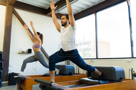 Photo for Instructor guiding a student through exercises on a pilates reformer in a studio - Royalty Free Image
