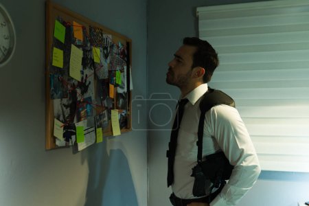 Detective stands attentively next to a corkboard filled with evidence and clues