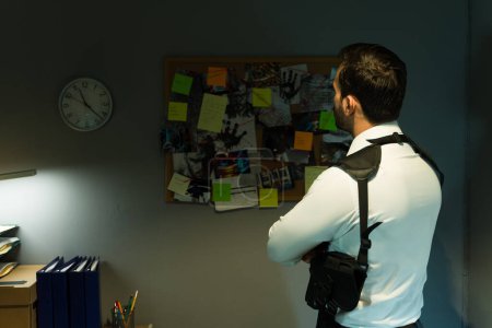 Foto de Detective enfocado analiza una pared de evidencia y conduce a una habitación oscura, resolviendo un caso pieza por pieza, visto desde la parte posterior - Imagen libre de derechos