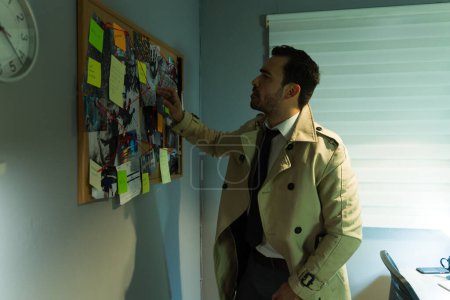 Focused private investigator examines evidence pinned to a corkboard in a dimly lit office