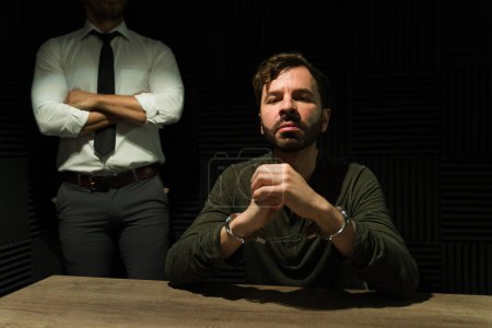 Foto de Detective decidido está detrás de un tenso sospechoso en el duro resplandor de un proyector en una sala de interrogatorios - Imagen libre de derechos