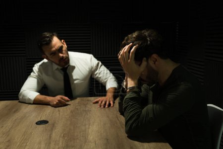 Photo for Detective conducts a focused interview with a distraught man in a dimly lit interrogation room - Royalty Free Image