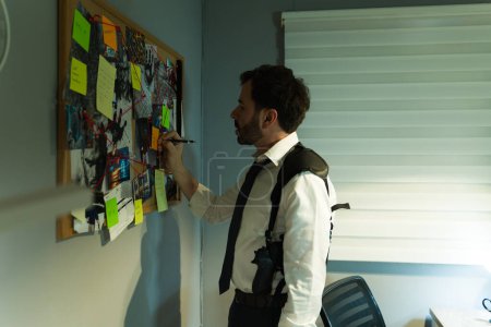 Profile view of private investigator carefully reviewing evidence and taking notes on a board, piecing together clues in a case