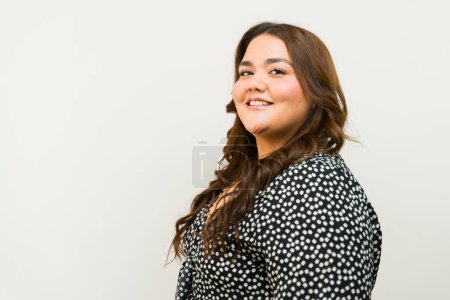 Confident plus-size woman striking a cheerful pose against a neutral background with some copy space