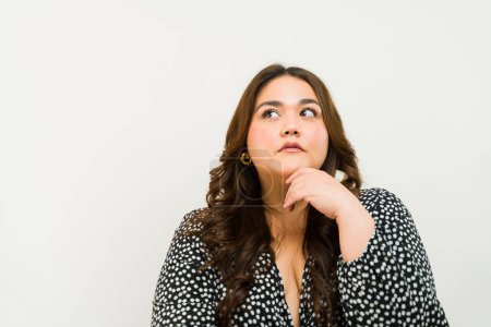 Photo for Confident plus-size woman with a contemplative expression against a neutral background with copy space - Royalty Free Image