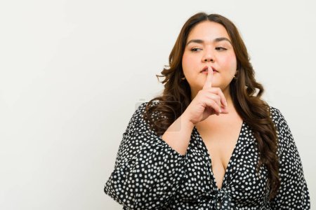 Plus-size woman with a finger on lips suggesting silence in a studio setting