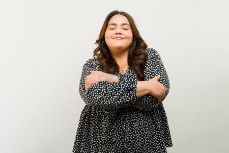Foto de Bonita mujer de talla grande con un abrazo como signo de autoestima en un estudio con fondo blanco - Imagen libre de derechos