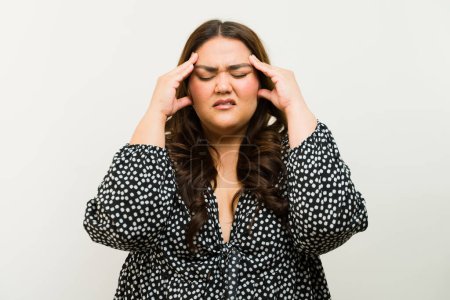 Foto de Mujer ansiosa de talla grande agarrándose la cabeza, mostrando síntomas de dolor de cabeza o migraña - Imagen libre de derechos