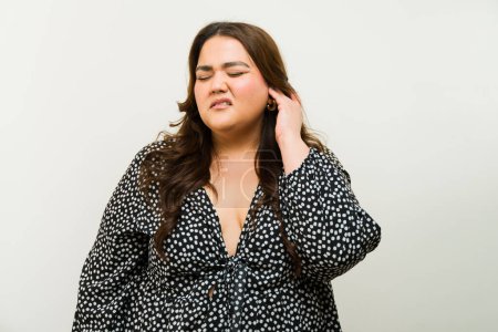 Foto de Mujer latina de talla grande tocándose la oreja y sintiendo algo de dolor e incomodidad sobre un fondo blanco - Imagen libre de derechos