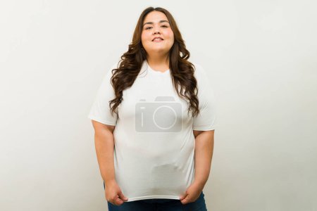 Foto de Alegre mujer hispana de talla grande posando con confianza en una camiseta blanca sobre un fondo de estudio - Imagen libre de derechos