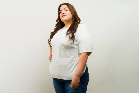 Photo for T-shirt mockup of a confident curvy plus-size woman striking a pose against a studio backdrop - Royalty Free Image