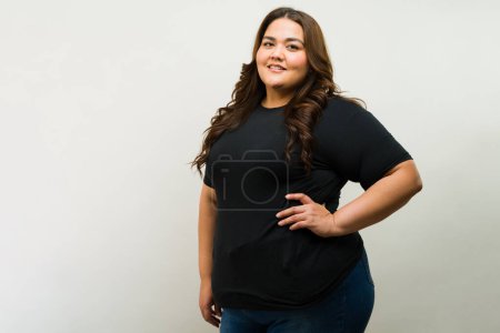 Foto de Burla de una mujer latina bastante curvilínea posando en un estudio mientras usa una camiseta negra - Imagen libre de derechos