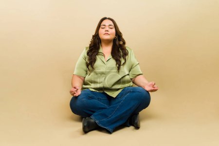 Foto de Mujer serena de talla grande en pose de loto medita con una expresión tranquila en un ambiente de estudio tranquilo - Imagen libre de derechos