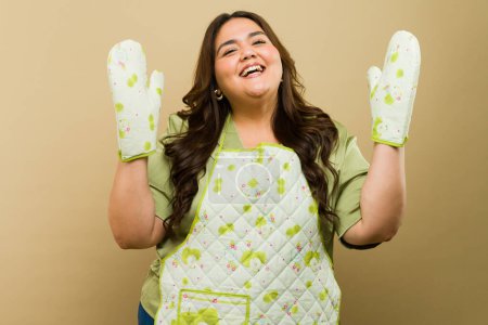 Foto de Mujer feliz plus-size preparado para hornear, vistiendo delantal adorable y guantes de horno en una configuración de estudio profesional - Imagen libre de derechos