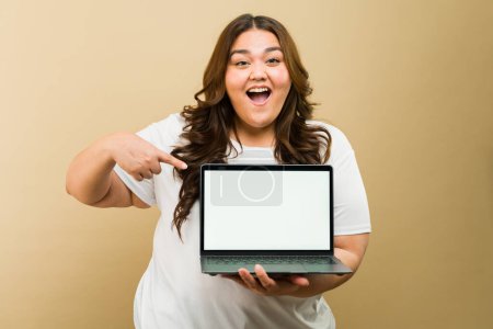 Foto de Mujer alegre sosteniendo un ordenador portátil con una pantalla simulada, ideal para el espacio publicitario - Imagen libre de derechos