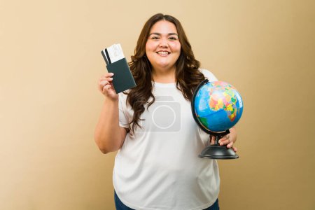 Photo for Beaming plus-size female with a passport and world globe, showcasing travel readiness and excitement - Royalty Free Image