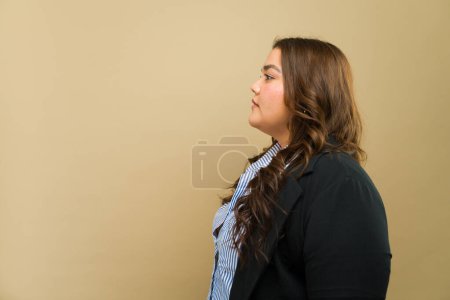 Foto de Vista de perfil de una mujer empoderada de talla grande vestida de forma formal, posando en un estudio - Imagen libre de derechos