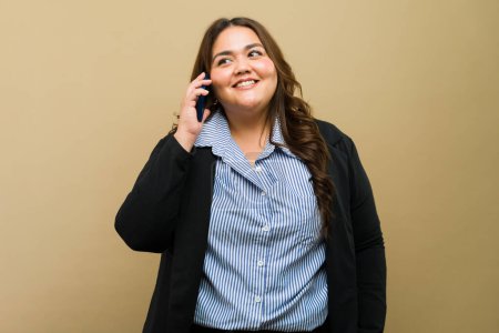 Foto de Mujer profesional de talla grande sonríe mientras mantiene una conversación agradable en su móvil - Imagen libre de derechos