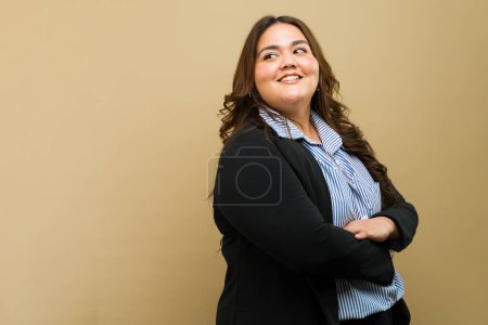 Téléchargez les photos : Femme confiante de grande taille en tenue professionnelle posant avec un sourire sur un fond beige - en image libre de droit