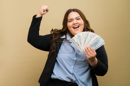 Mujer feliz plus-size radiante y la celebración de dinero, regocijándose en su éxito financiero en un ambiente de estudio profesional