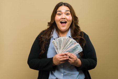 Photo for Happy plus-size woman posing with a bundle of money in the studio - Royalty Free Image