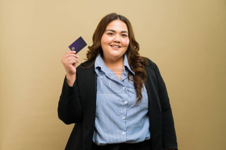 Foto de Orgullosa mujer de negocios de tamaño grande mostrando con confianza una tarjeta de crédito con una sonrisa en un entorno de estudio - Imagen libre de derechos