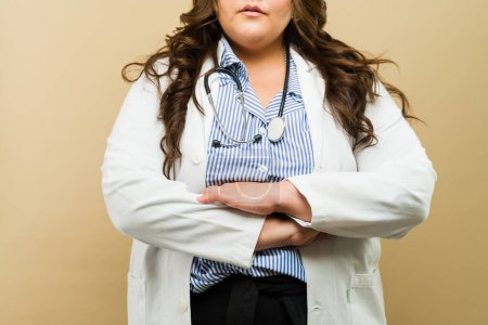Porträt einer kurvigen Ärztin in Labormantel und Stethoskop, die in einem professionellen Studio-Setting posiert