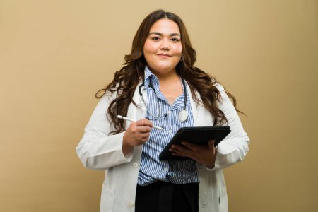 Foto de Profesional médico con atuendo de talla grande posando con una tableta y un bolígrafo digital en un entorno de estudio - Imagen libre de derechos