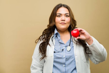 Photo for Female doctor of plus size holding a red heart, symbolizing compassion and heart health - Royalty Free Image