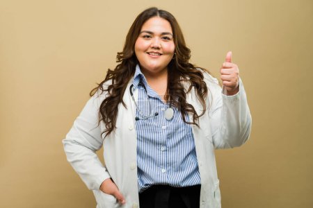 Foto de Retrato de una doctora de talla grande posando con un gesto de pulgar hacia arriba en un ambiente de estudio - Imagen libre de derechos