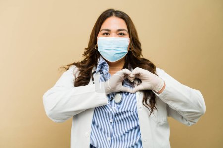Plus-size female doctor exuding confidence while wearing a mask and making a heart gesture with her hands