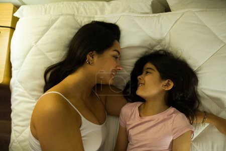 Téléchargez les photos : Moment touchant entre une mère et sa fille alors qu'ils partagent un regard aimant dans le confort de leur chambre la nuit - en image libre de droit