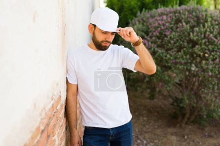 Téléchargez les photos : Jeune homme hispanique avec une barbe portant un t-shirt blanc et un bonnet, parfait pour mettre en valeur les modèles de marque, debout à l'extérieur - en image libre de droit