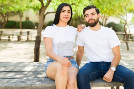 Foto de La pareja latina en su juventud que usa camisetas blancas simples se sienta junta, proporcionando una plantilla de maqueta ideal para sus requisitos de diseño - Imagen libre de derechos
