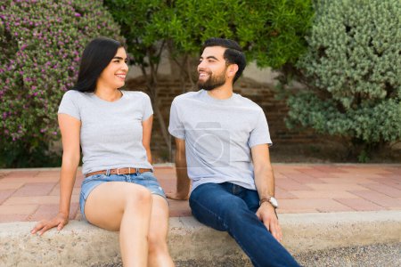 Spanisches Paar in passenden grauen T-Shirts lächelt und genießt einen glücklichen Moment zusammen in einer friedlichen Gartenkulisse