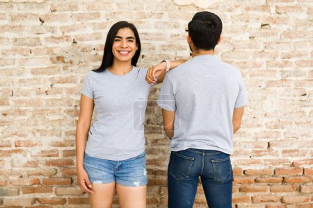 Photo for Cheerful young hispanic couple wearing blank gray t-shirts ready for branding, standing against a rustic brick wall background - Royalty Free Image