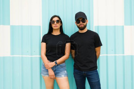 Foto de Pareja latina segura con camisetas negras en blanco y ropa casual posando sobre un vibrante fondo azul para una plantilla de diseño simulada - Imagen libre de derechos